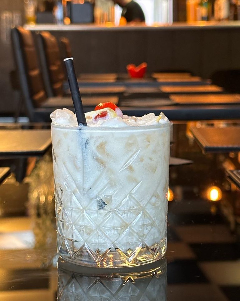 a white cocktail in a tumbler with straws